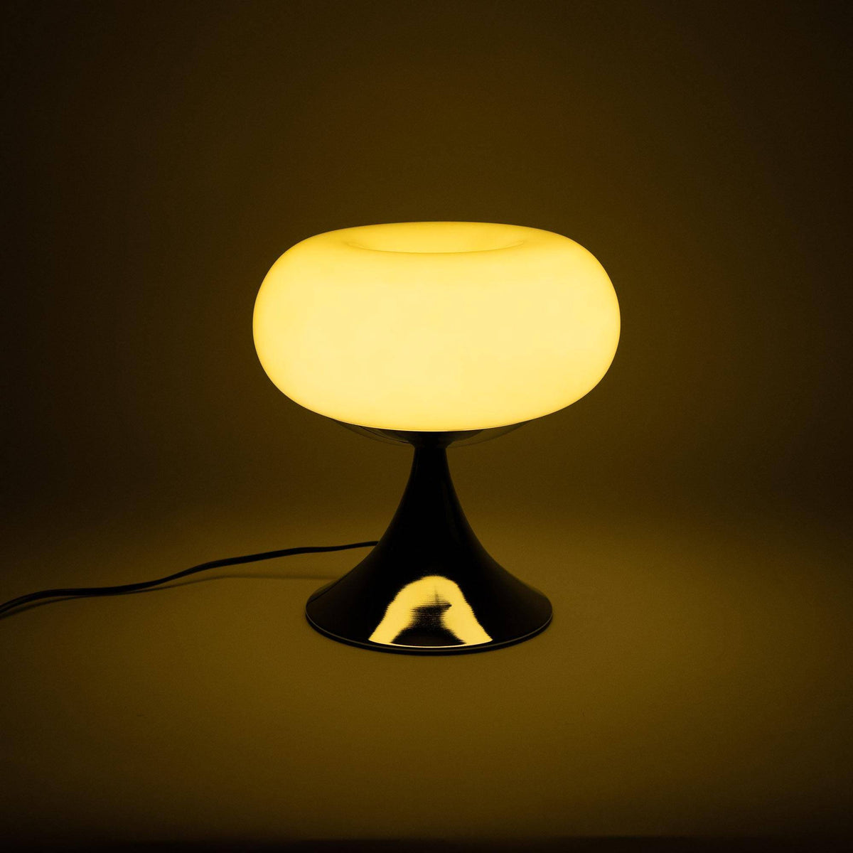 Retro bordlampe tændt, udsender varmt lys gennem sin ecru farvede glasskærm. Perfekt til hyggelig belysning i hjemmet med 60&#39;er æstetik.