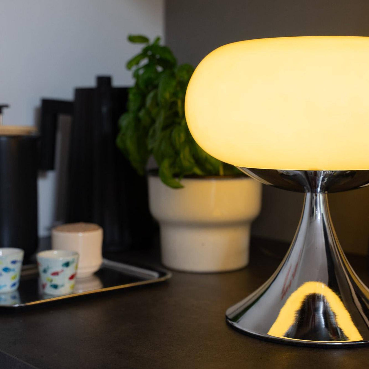 Vintage bordlampe med skinnende metalfod og ecru glasskærm lyser op i et moderne køkkenmiljø. Perfekt som dekorativ belysning.