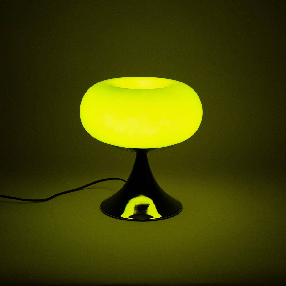 Vintage inspireret grøn bordlampe tændt i mørke, udsender en varm glød. Perfekt som stemningsbelysning i hjemmet.