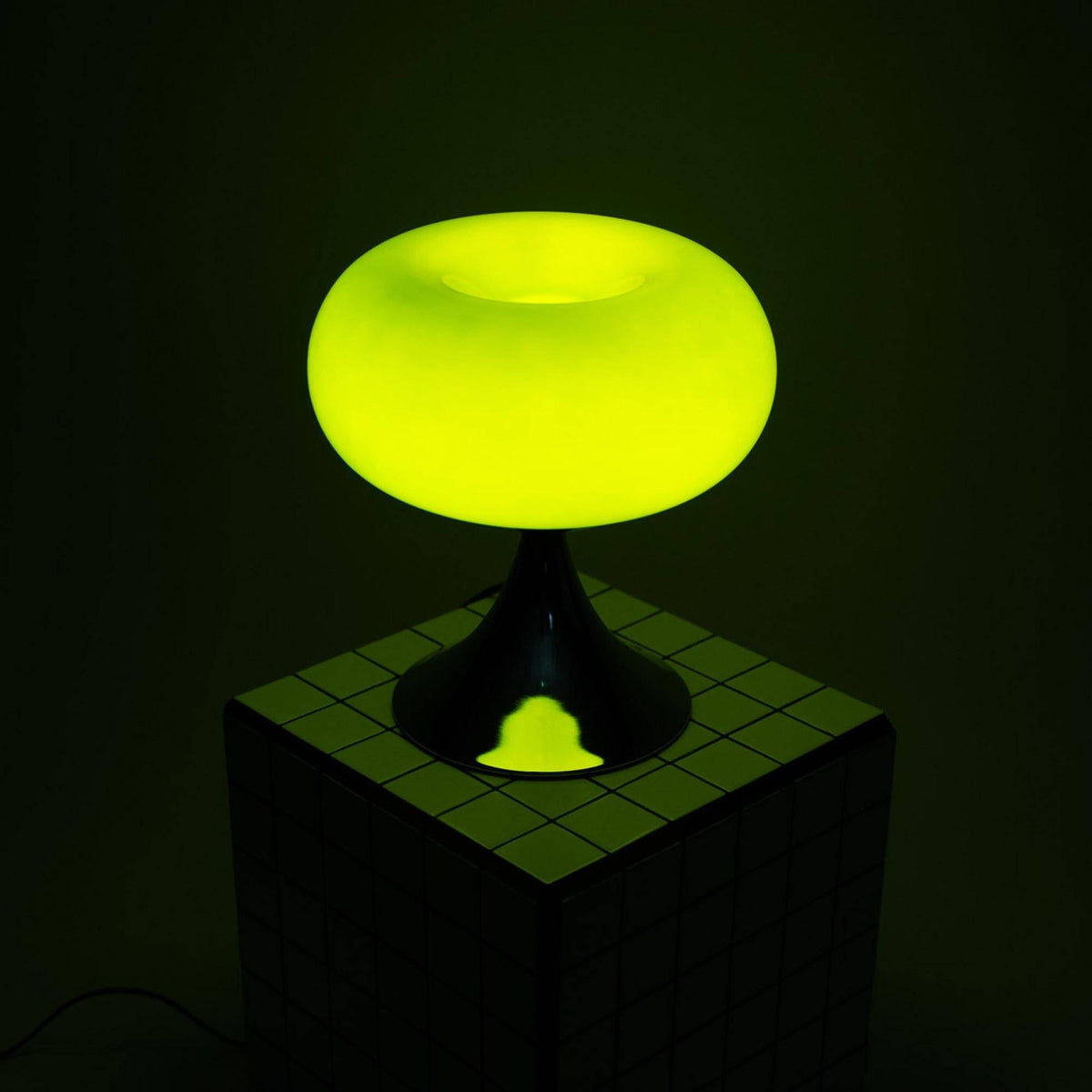 Tændt grøn retro bordlampe på et geometrisk mønstret bord, skaber en hyggelig atmosfære i rummet.