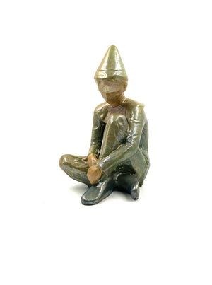 Green ceramic figure of a seated boy, created by Giordano Tronconi